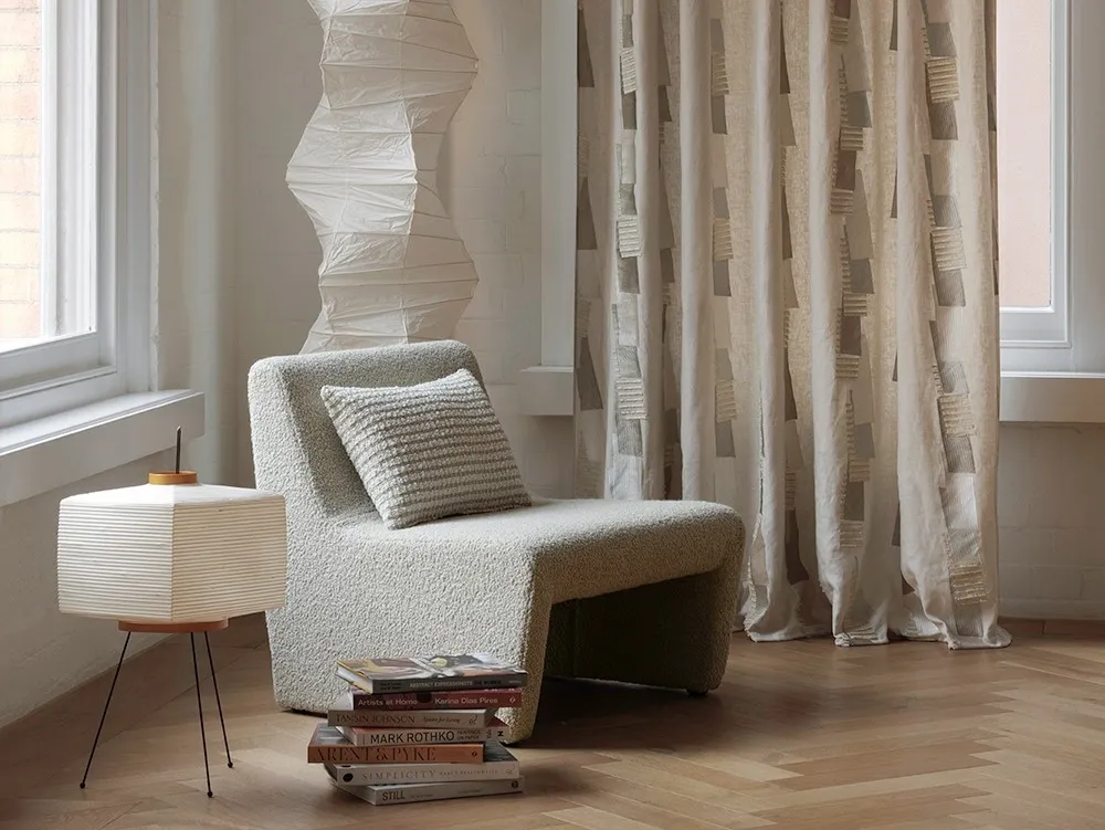 Patterned curtains beside a bouclé lounge chair and paper floor lamp