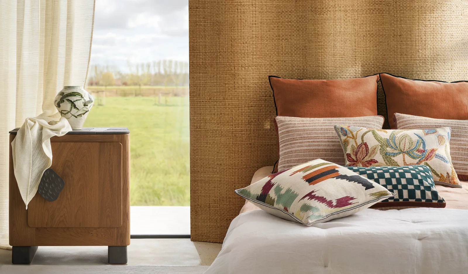 Bed with embroidered cushions against a woven grasscloth wall